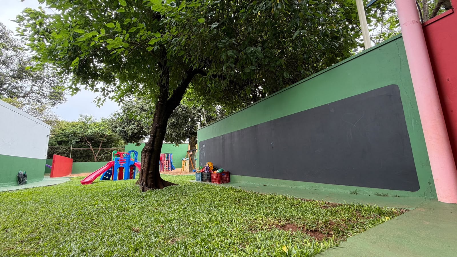 Área gramada com árvore, brinquedos e lousa externa