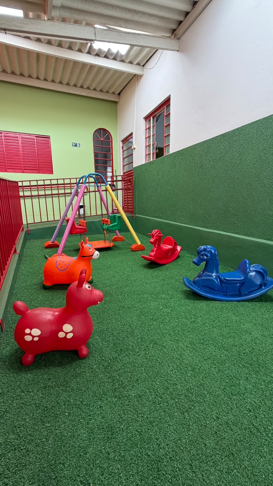 Balanços e cavalinhos no parque coberto com piso verde